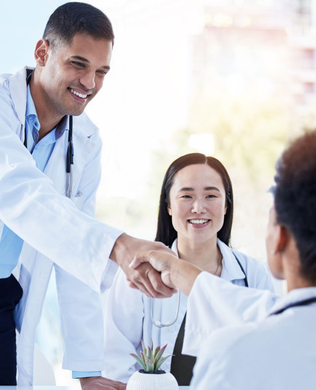Two physicians shake hands while a colleague looks on