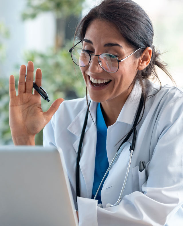 A smiling physician on a video call at a laptop