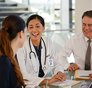 A physician and colleagues talk around a table in a bright office
