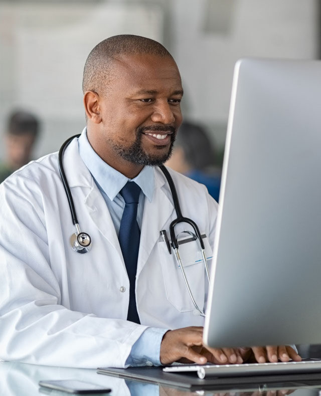 A smiling physician working at a desktop computer