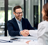 A physician and a practice leader shake hands across a desk