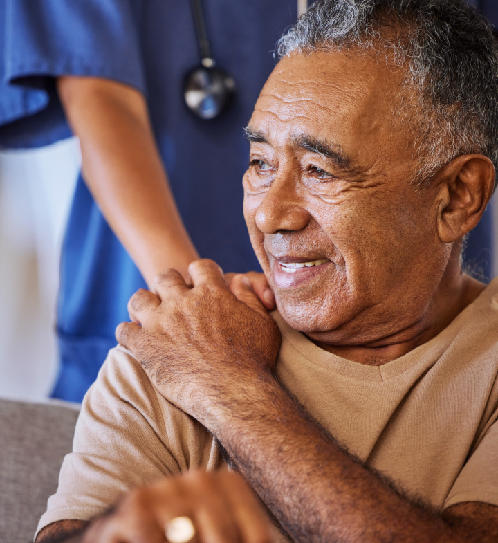 An older patient in conversation with a clinician who has a hand on his shoulder.