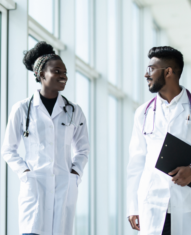Two clinicians walking together through a light-filled clinical corridor.