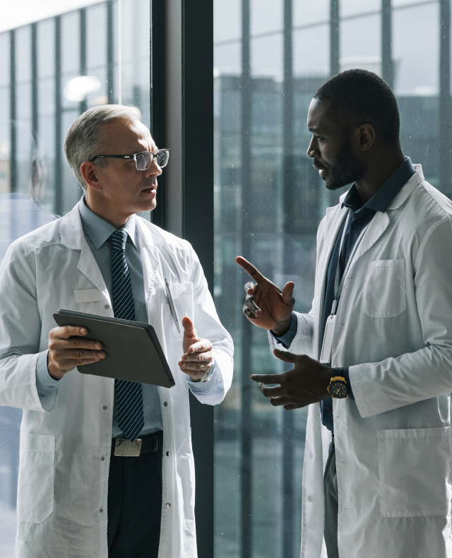 Two physicians in conversation beside a window.